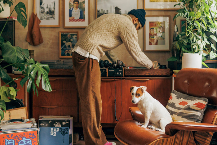 Photo image of a man playing records in his apartment with his dog listening.
